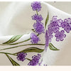 Nahaufnahme eines cremefarbenen Stoffes mit lila Lavendel-Blumendickunst und grünen Blättern