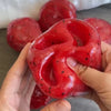 Une main tient un jouet anti-stress en slush de pastèque rouge vif avec une surface texturée.