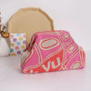 A pink and orange hand-knit clutch bag with geometric patterns rests in front of a beige fabric backdrop.