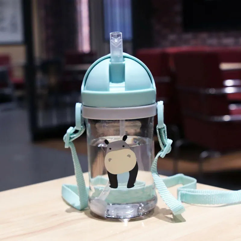 A clear sippy cup with a light blue lid and straw, featuring a cute bear design, resting on a wooden surface.