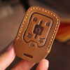 A brown leather key fob case with stitching and a cutout for a key is held in a hand.