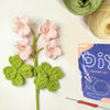 A beginner crochet kit featuring pink flowers and green leaves, along with yarn and a crochet needle.