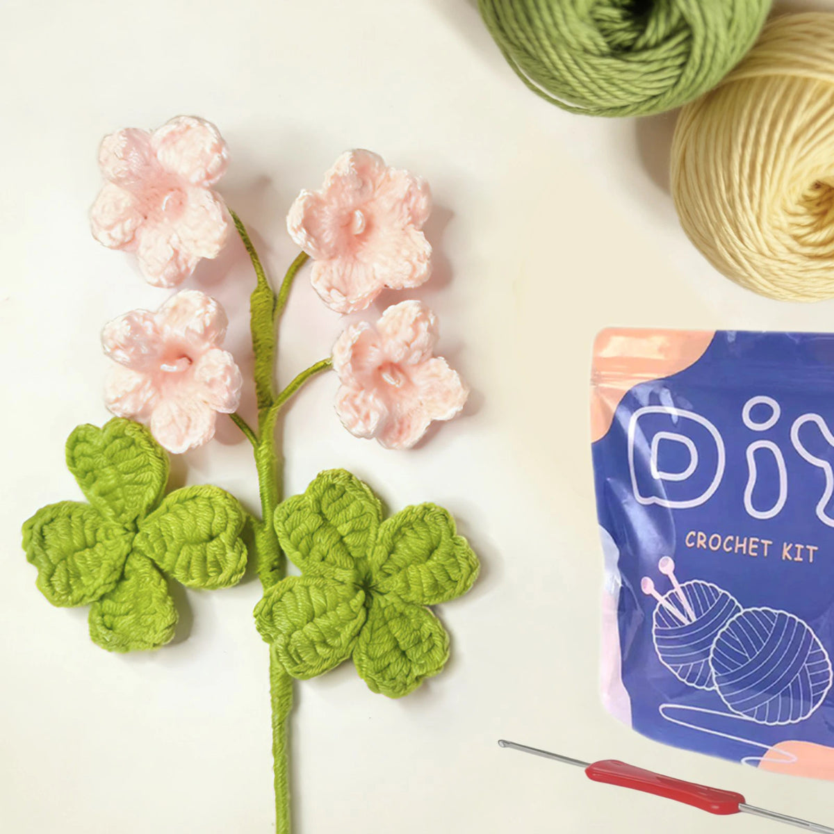 A beginner crochet kit featuring pink flowers and green leaves, along with yarn and a crochet needle.