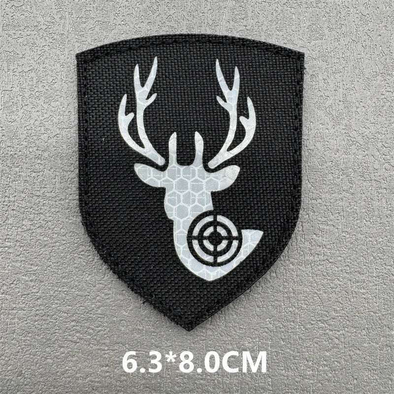 A black shield-shaped patch featuring a white deer antler silhouette with a crosshair target design.