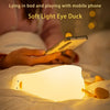 A soft light eye duck night light illuminates a hand holding a mobile phone in a bedroom setting.