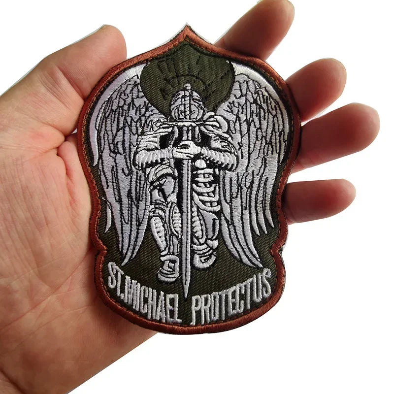 A stitched patch featuring an archangel design with wings and the name St. Michael Protectus on a dark green background.