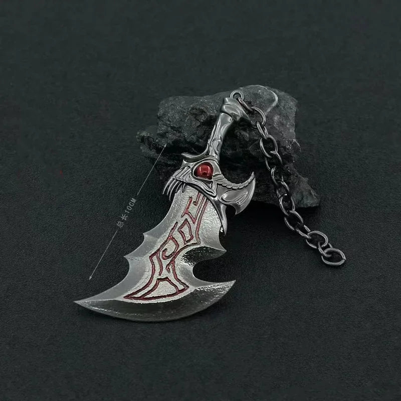 A silver metal sword keychain with an ornate hilt and red gem, resting on a dark rock.