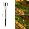 A silver and black solar powered garden lantern light mounted on a stake, illuminating a pathway in a grassy garden.
