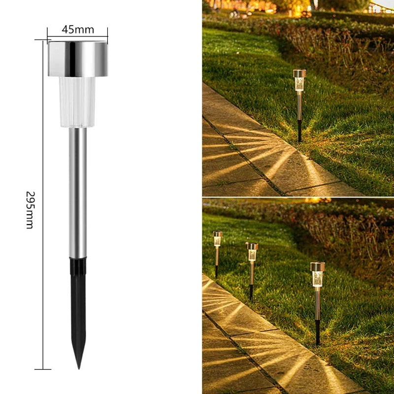 A silver and black solar powered garden lantern light mounted on a stake, illuminating a pathway in a grassy garden.