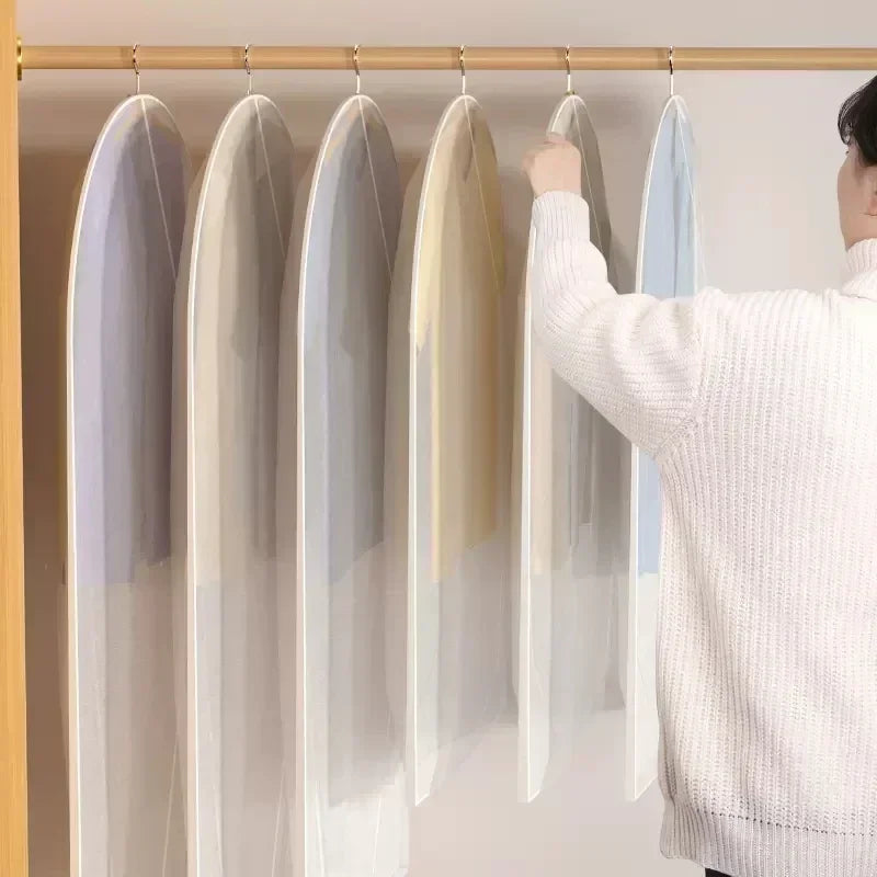 A person is hanging transparent zippered garment storage bags on a wooden rod.
