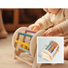 A baby is interacting with a wooden rattle bell toy designed for soothing sounds.