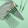 A set of thirteen makeup brushes in various shades of green and beige are displayed next to a gray fabric travel bag.