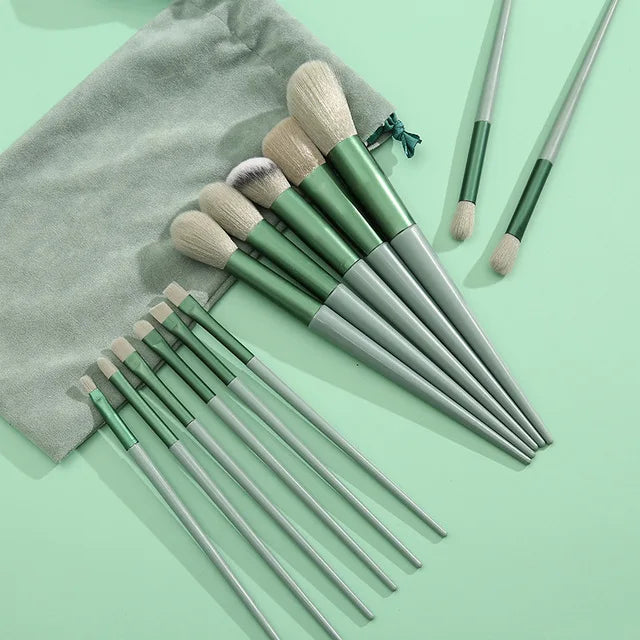 A set of thirteen makeup brushes in various shades of green and beige are displayed next to a gray fabric travel bag.