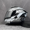 A silver modular flip-up motorcycle helmet is displayed against a gray stone background.