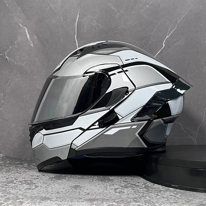 A silver modular flip-up motorcycle helmet is displayed against a gray stone background.