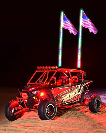 A red Can-Am Maverick X3 off-road vehicle with illuminated American flags mounted on the roof at night.