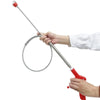 A hand is operating a drain unclogging tool with an ergonomic handle, showing the long metal probe and coiled end.
