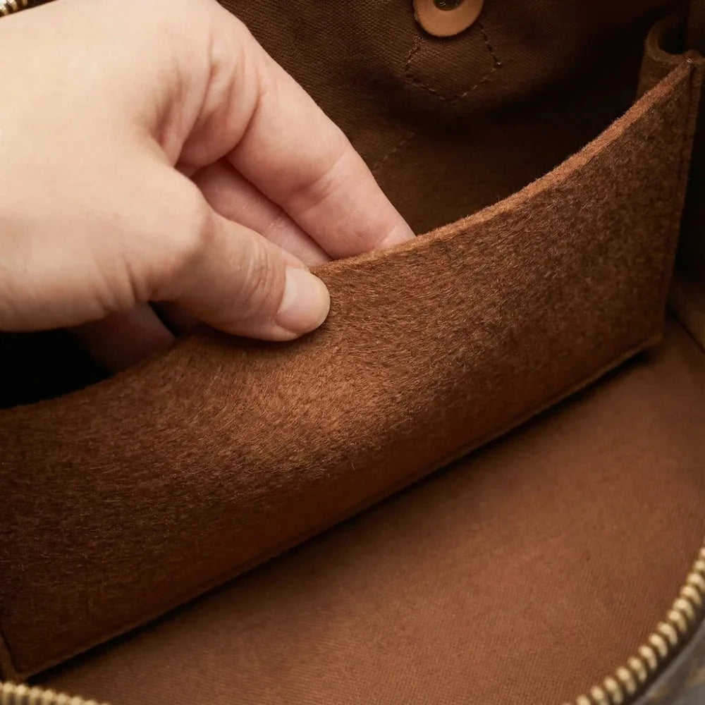 A hand is opening a brown felt bag organizer insert with a zipper pocket.