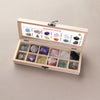 A wooden gift box containing twelve natural gemstone crystals arranged in compartments with an informational label.