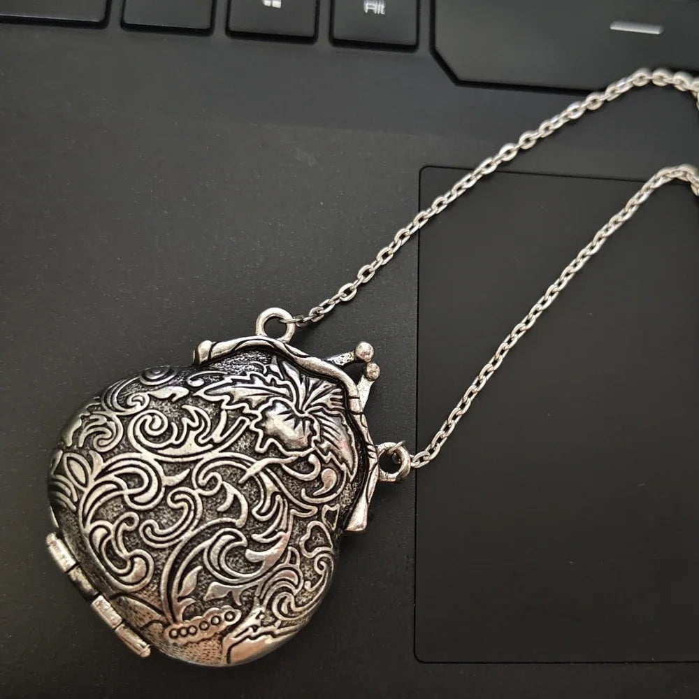 A detailed retro bronze mini locket pendant hanging from a silver chain, resting on a black keyboard.