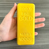 A hand holds a yellow butter fidget stick labeled 999.9 Fine Gold with a net weight of 1000g.