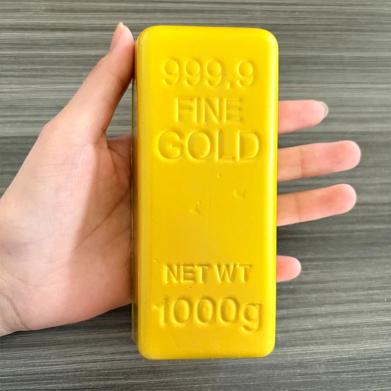 A hand holds a yellow butter fidget stick labeled 999.9 Fine Gold with a net weight of 1000g.