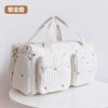 A cream-colored embroidered cotton diaper bag featuring a quilted pattern and delicate pink floral designs.