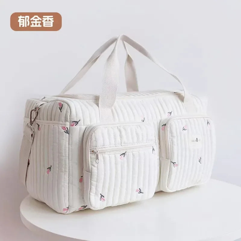 A cream-colored embroidered cotton diaper bag featuring a quilted pattern and delicate pink floral designs.