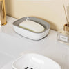 A white double-layer draining soap dish with a non-slip base is shown on a light surface.