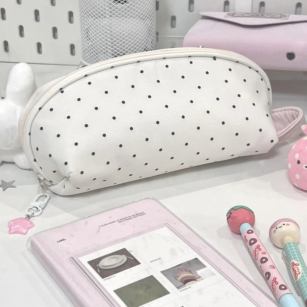 A white polka dot shell-shaped pencil case is shown next to a pink cosmetic bag and a pink pencil case.