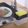 A hand is using a green sponge to clean a plate under a faucet in a kitchen sink, near a yellow foam soap dispenser.