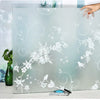 A sheet of frosted privacy window film with a white floral and swirl pattern is displayed on a table.