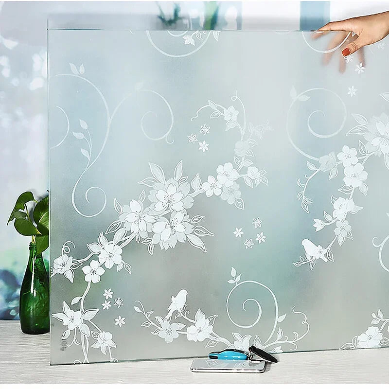 A sheet of frosted privacy window film with a white floral and swirl pattern is displayed on a table.