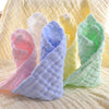 A stack of three soft natural cotton muslin baby washcloths in pink, blue, and green are displayed on a yellow textured surfa