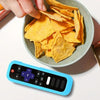 A hand is holding a bowl of crispy yellow chips next to a blue silicone TV remote cover.