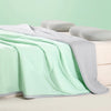 A light mint green ice silk cooling blanket is draped over a white surface next to two gray pillows.