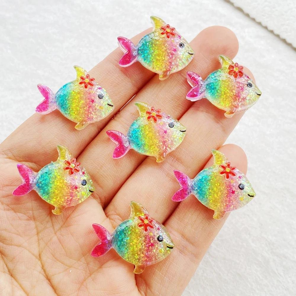 A hand holds several iridescent, colorful resin charms shaped like small fish.