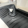 A close-up view of a silicone faucet splash mat used to catch water, placed on a black kitchen surface.