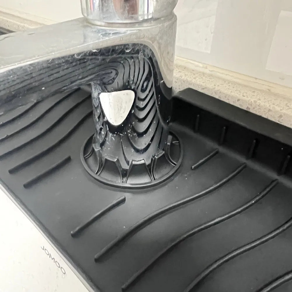 A close-up view of a silicone faucet splash mat used to catch water, placed on a black kitchen surface.