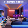 A hand holds an IR remote control for a smart app-controlled RGB LED strip light system in a modern living room.