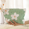 A light green floral corduroy makeup bag with a white daisy pattern is held by a hand.
