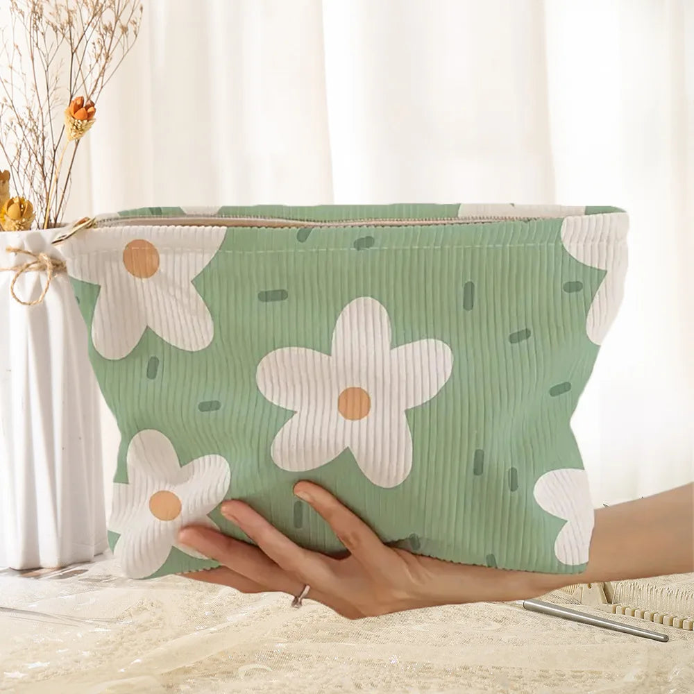 A light green floral corduroy makeup bag with a white daisy pattern is held by a hand.