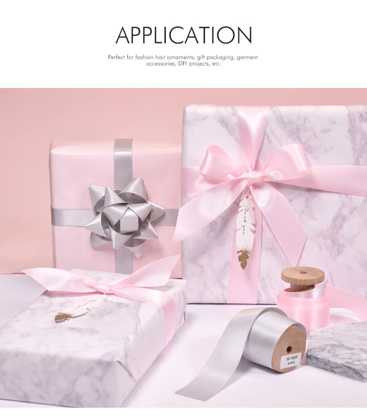 Pink satin ribbon rolls and gift packaging with silver ribbons displayed on a white marble surface.