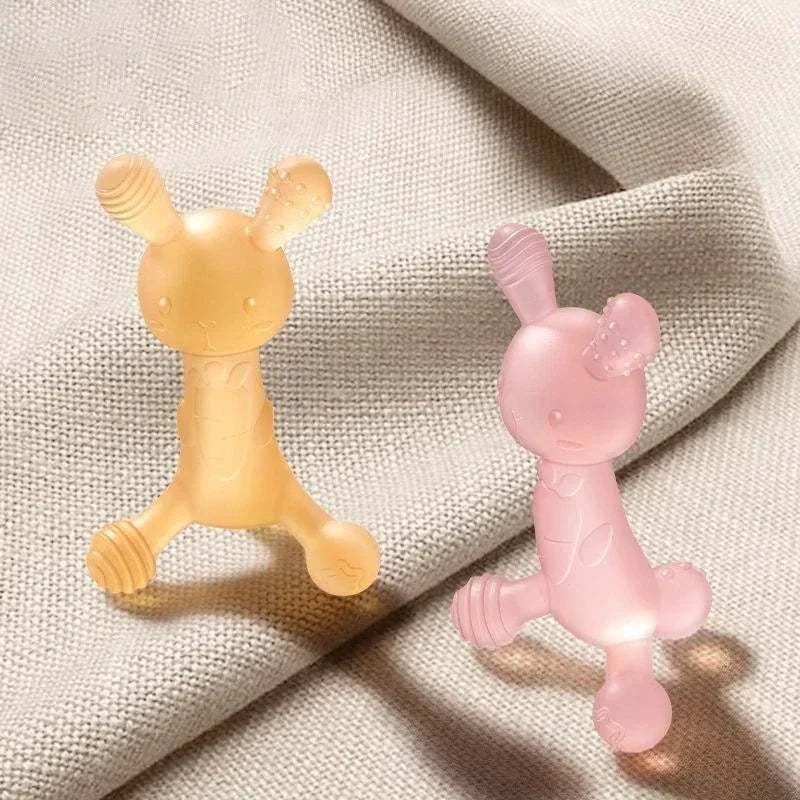A silicone cartoon rabbit teether in pale yellow and pink colors resting on a light fabric.