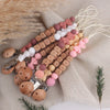 A collection of personalized silicone pacifier clips and a floral-themed lanyard arranged on a beige fabric.