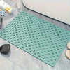 A green anti-slip shower mat with numerous drainage and massage holes placed on a gray tiled surface.