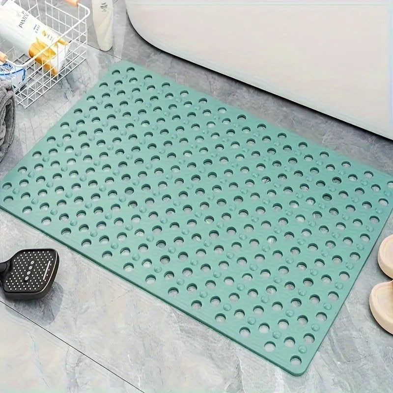 A green anti-slip shower mat with numerous drainage and massage holes placed on a gray tiled surface.