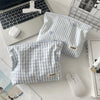 A light blue and white striped makeup bag with floral embroidery is shown next to a laptop and a wireless mouse.