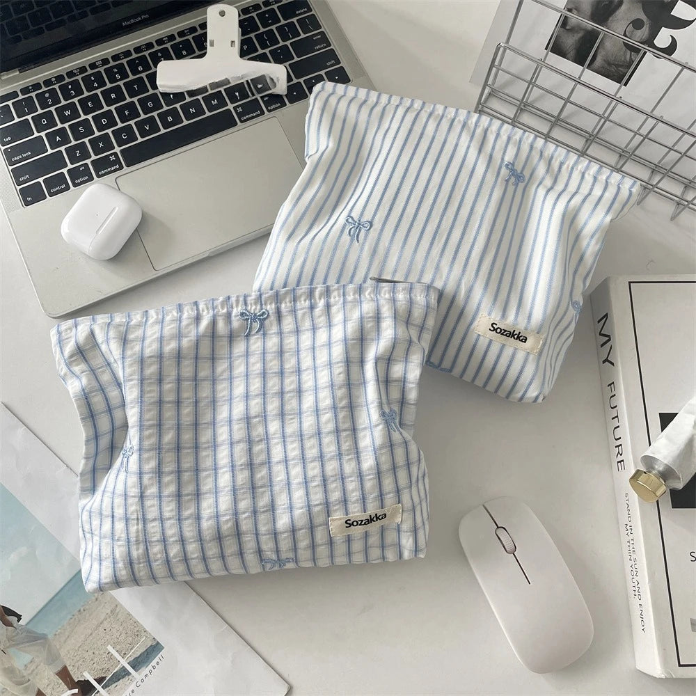 A light blue and white striped makeup bag with floral embroidery is shown next to a laptop and a wireless mouse.