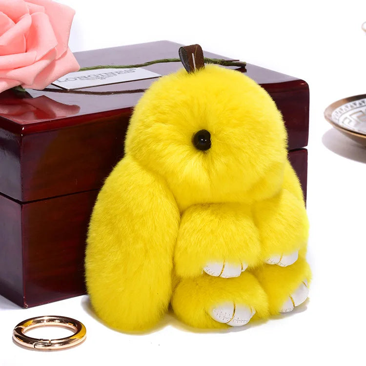 A fluffy yellow angel bunny keychain with a black pom pom tail resting on a dark wooden box.